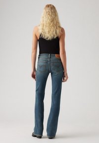 Jean en denim bleu évasé à taille haute, doté de poches arrière avec détails cousus et d'une étiquette en cuir marron à la taille.