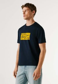 T-shirt in cotone blu navy con grafica etichetta vintage gialla con la scritta "Pipe Jeans London" sul davanti, scollo rotondo, maniche corte.