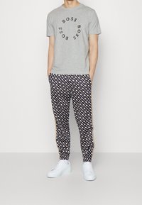 Šedé tričko s krátkým rukávem a černým logem "BOSS", doplněné o tmavě modré joggers s vzorem a krémovými akcenty a bílými teniskami.