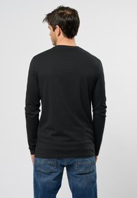 T-shirt nera a maniche lunghe, materiale in cotone, vestibilità comoda, collo girocollo, cuciture decorative sulle spalle, indossato con jeans blu, schiena visibile.