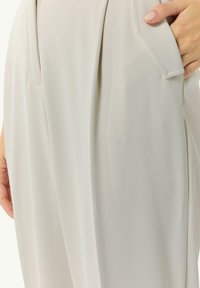 Jasnoszare spodnie z gładkiego materiału, z plisowanym fasonem, bocznymi kieszeniami i dopasowanym w pasie. Prosty i nowoczesny krój z czystymi liniami.