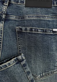 Denim jeans in een vervaagde blauwe kleur. Kenmerken zijn onder andere een achterzak met stiksels en een zwart merklabel op de tailleband. De textuur is glad.
