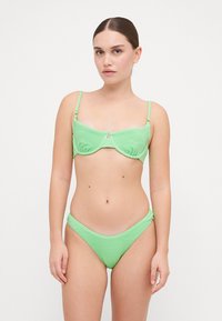 Zöld bikini, textúrált anyagból, amely szerkezetes, drótos melltartóval és magas derekú alsó résszel rendelkezik, kontrasztos díszítéssel.