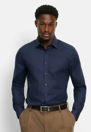 Navy blue long-sleeve shirt with a subtle pattern, button-down collar, and matching buttons, paired with tan trousers and a brown belt.