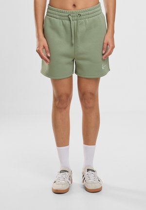 Bas du corps d'une personne portant un short vert clair à cordon, des chaussettes blanches et des baskets blanches Adidas avec des rayures noires.