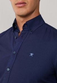 Marineblauw overhemdd met een slim fit, featuring een klein lichtblauw geborduurd logo op de linker borst en contrasterende knopen.