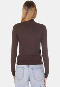 Maglione marrone aderente con maniche lunghe, polsini e orlo a coste, realizzato in materiale morbido. Indossato con jeans in denim chiaro, visto da dietro.