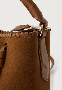 Καφέ σουέντ τσάντα χειρός με δερμάτινες λεπτομέρειες, διαθέτει ραμμένα χείλη και μεταλλικό κούμπωμα. Η υφή φαίνεται απαλή με λουράκι λείο.