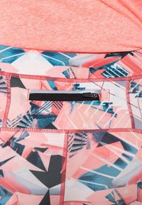 Różowe legginsy sportowe z geometrycznym wzorem w niebieskim i czarnym kolorze, z czarną kieszenią na zamek oraz kontrastowymi szwami wzdłuż krawędzi.