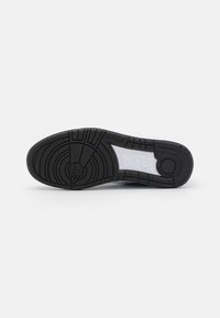 Suela de sneaker Nike en goma negra, con un patrón circular cerca del talón y una banda de rodadura texturizada para agarre. Logo blanco en la entresuela.