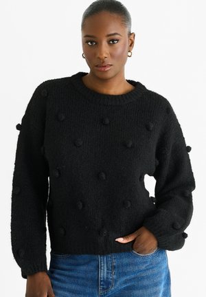 Black knitted sweater with puffed polka dot accents, round neckline, and long sleeves. Fabric shows a textured finish, fitted at the waist.
