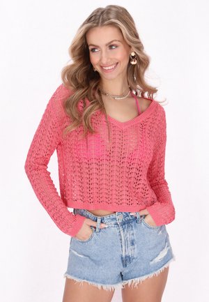 Maglione cropped rosa lavorato a maglia con scollo a V e maniche lunghe, abbinato a pantaloni shorts in denim chiaro con effetto sfrangiato.