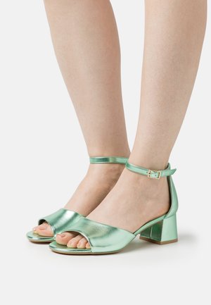 Muntgroene metallic blokhak sandalen met open neuzen, enkelbandje met een gesp en een gladde textuur op de bovenkant.