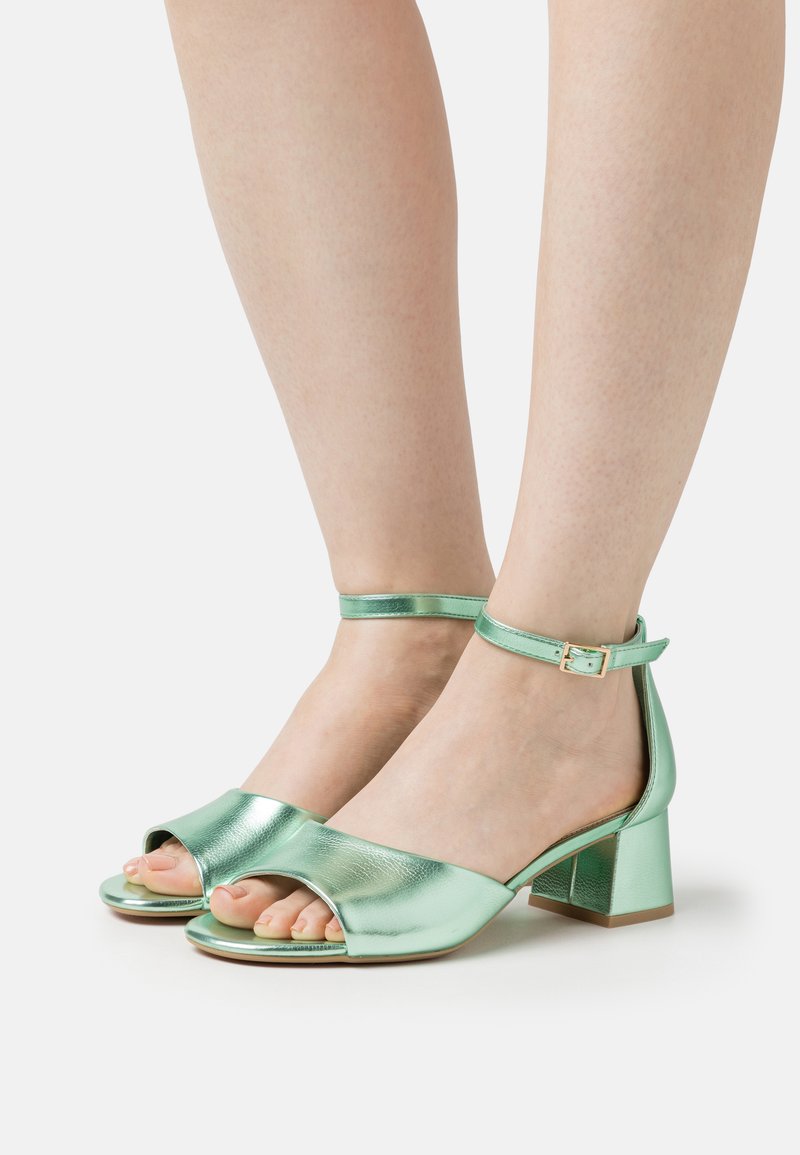 Mintgröna metalliska blockklackssandaler med öppen tå, ankelrem med spänne och en slät texturerad ovandel.