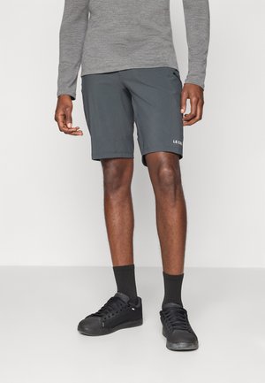 Shorts de sport gris foncé pour homme, fabriqués à partir d'un tissu léger, avec une coupe décontractée et des détails de logo sur le côté, associés à des baskets noires.