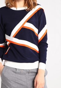Marinblå tröja med diagonala vita och orangea ränder, rundad halsringning, ribbade ärmslut och nederkant, tillverkad av ett mjukt stickat material.