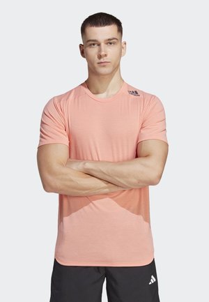 Short-sleeve coral athletic shirt with a round neckline, soft texture, and subtle gradient pattern. Features a small logo on the left shoulder.