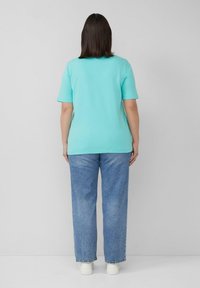 Mintgroene T-shirt met korte mouwen van zachte katoen, gecombineerd met lichtblauwe, loszittende jeans en witte sneakers, gezien van achteren.