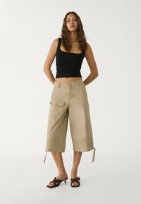 Khaki cargo pants with two side pockets, drawstring hems, and a relaxed fit. Paired with a black fitted tank top and heeled sandals.