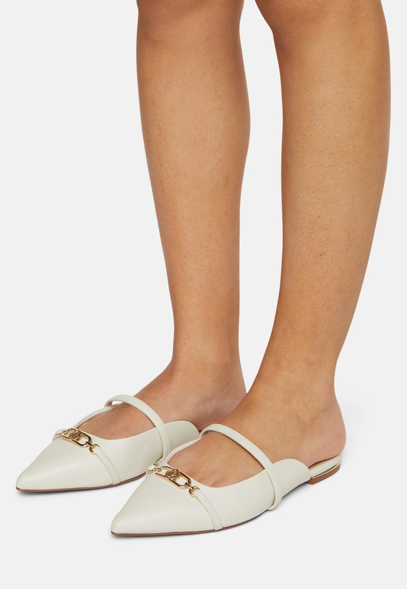 Mules en cuir blanc avec des bouts pointus, présentant un design à double bride et un accent en chaîne dorée à l'avant. Semelle plate. Texture lisse.