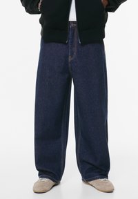 Wijdvallende denim jeans in donkerblauw, met contrasterende stiksels en een klassieke ritsluiting. Gelaagd stof met een subtiele glans.