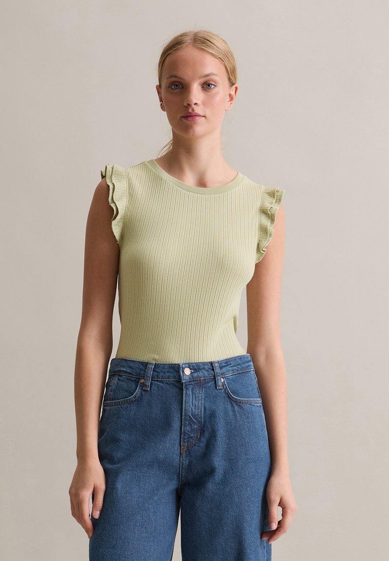 Jasnozielony prążkowany top na ramiączkach z falbankami na ramionach, zestawiony z niebieskimi jeansami o wysokim stanie. Prosty i czysty design bez widocznych wzorów.