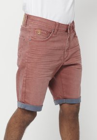 Shorts en denim rouge avec un ourlet bleu replié, dotés de cinq poches, d'une fermeture à bouton en métal et d'une étiquette en cuir de la marque sur la taille.