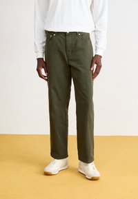 Pantalons droit en vert olive en toile de coton, dotés d'un design classique à cinq poches et de quincaillerie en ton argent, associés à des baskets blanches.