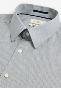 Light gray patterned shirt featuring a spread collar, two white buttons, and a label with "NEXT SIGNATURE" inside the neckline.