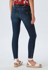 Jeans ajustados de un azul oscuro con una textura suave y detalle de cremallera en el tobillo. Presenta dos bolsillos traseros con costuras en contraste.