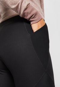Svarta leggings med en slät yta, försedda med en sidoficka och kontrasterande sömmar. Matchade med en strukturerad ljusrosa tröja.