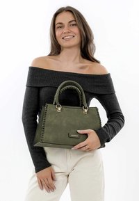 Green faux leather handbag with gold hardware, stitched detailing, structured shape, and dual handles, held by a person in casual attire.