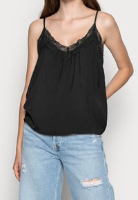 Camiseta negra sin mangas con encaje, con tirantes finos ajustables y un corte holgado, combinada con jeans azul claro desgastados.