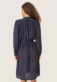 Marineblaue Kleid aus leichtem Stoff, mit langen Ärmeln, tailliertem Schnitt und einer leicht durchsichtigen Textur am Saum.