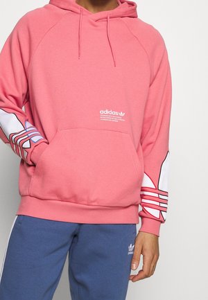 Sudadera rosa con un bolsillo tipo canguro y el logo blanco de Adidas. Cuenta con mangas con un diseño estampado en azul y rojo. Material suave de felpa.