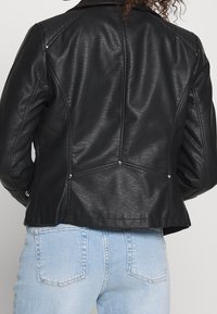 Svart läderjacka med en åtsittande silhuett, synliga sömmar, silverdetaljer och en klassisk krage, sedd från baksidan.