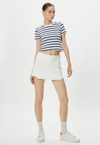 Randig bomullscrop-top i marinblått och vitt, matchad med en vit mini kjol. Modellen bär vita sneakers och ankelsockar.