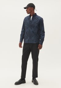 Cămașă cu model floral marin, cu un croi relaxat, asortată cu pantaloni negri. Accesoriile includ o șapcă neagră și mocasini negri.