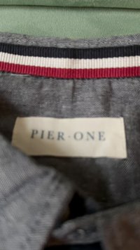 Riide silt, millel on "PIER ONE" tekst, on õmmeldud halli rõivasse, millel on punane, valge ja must triibuline krae.