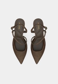 Escarpins marron en daim avec talon slingback, bout pointu, brides à la cheville et semelle intérieure rembourrée. Présentent un logo doré sur la semelle intérieure.