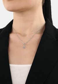 Silver halsband med en dekorativ solstrålependel, med en kedjedesign. Bärs över en ljus topp, kompletterad av en svart kavaj.
