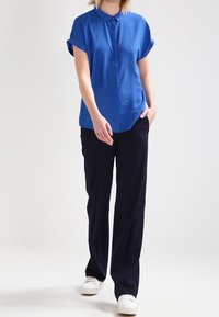 Blå kortärmad skjorta med krage, i kombination med marinblå byxor och vita sneakers. Slät tygkvalitet, avslappnad passform, upprullade ärmar.