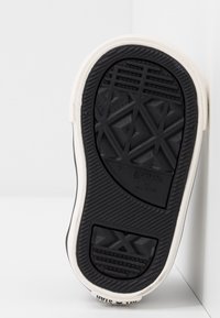 Czarna gumowa podeszwa z fakturowanym wzorem antypoślizgowym, z białą ścianką boczną i logiem "Converse All Star" z tyłu.