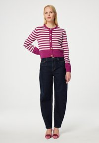 Paarse en witte gestreepte cardigan met ronde hals en knoopsluiting, gecombineerd met hooggewaisted donkerblauwe jeans en roze hartvormige hakken.