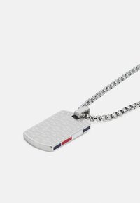 Pendentif en forme de plaque militaire en argent avec un motif texturé, arborant des accents bleus, blancs et rouges d'un côté, attaché à une chaîne en argent.