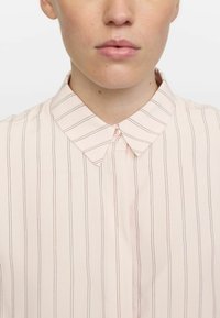 Light pink button-up shirt with thin vertical stripes. Features a classic collar and a soft, smooth texture. Button closure at neck.