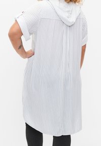 Robe chemise rayée en gris clair et blanc, dotée d'une capuche, de manches courtes et d'un ourlet asymétrique. Texture de tissu douce.