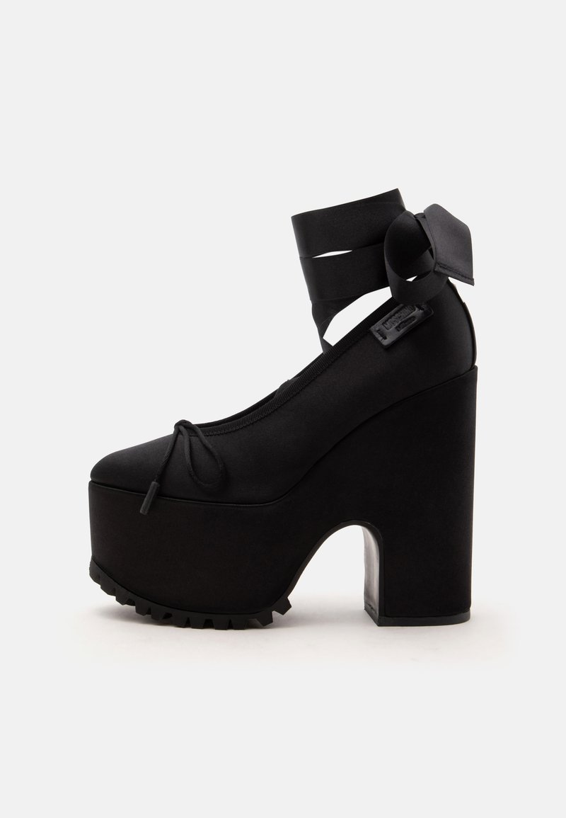 Chaussure noire à plateforme avec talon épais, bout arrondi, brides autour de la cheville et détails en dentelle sur la partie supérieure.