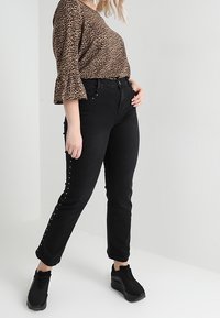 Haut à imprimé léopard avec manches à volants, jean noir taille haute avec boutons latéraux, et baskets noires. Tissu lisse et coupe ajustée.