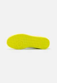 Lacoste sneaker sole, bright yellow, textured with small squares, featuring a circular accent in the center, provides traction and support.